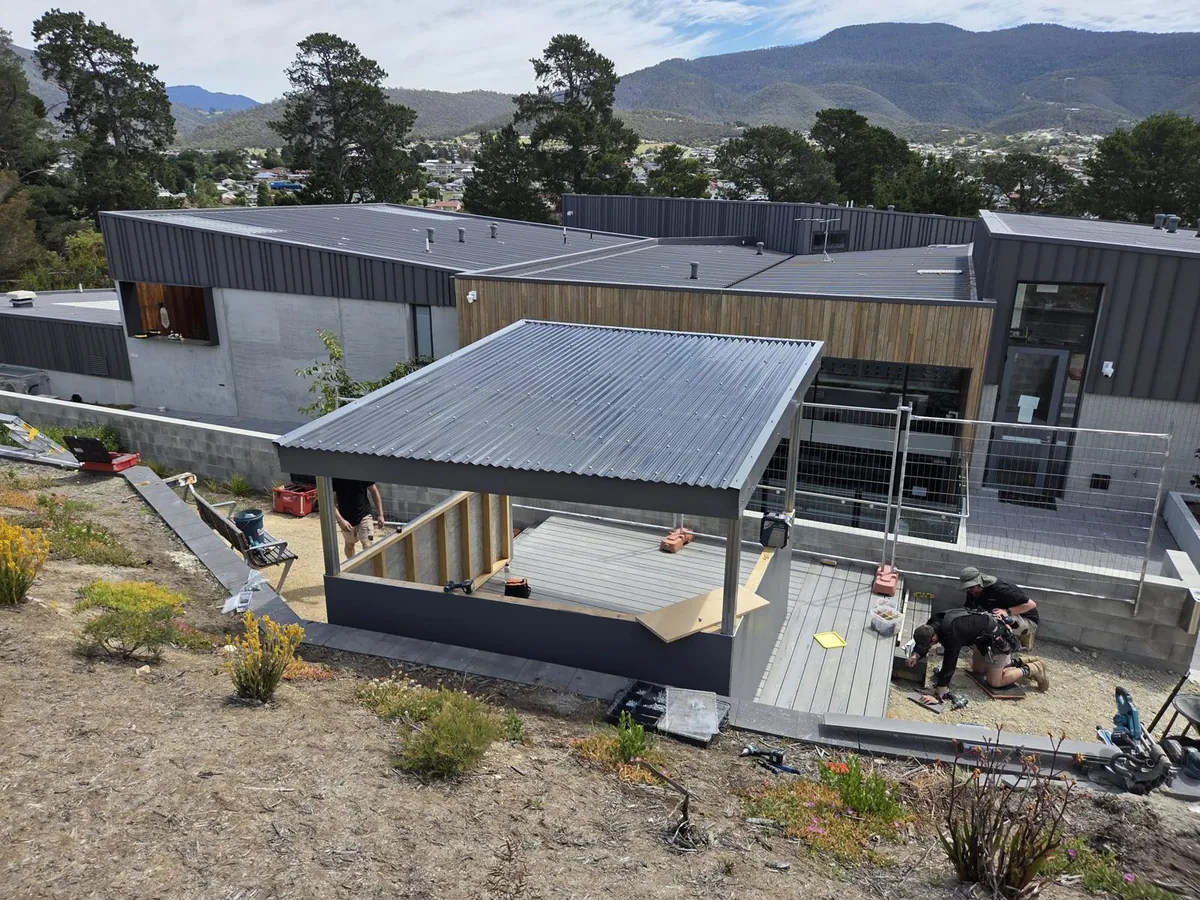 New community housing units with timber cladding and a covered deck, hills behind