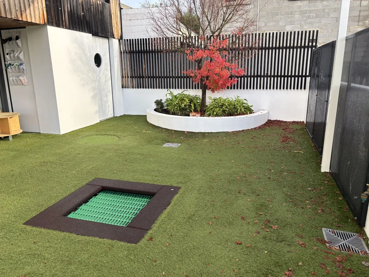 Early learning centre play yard with in-ground trampoline and soft-fall turf